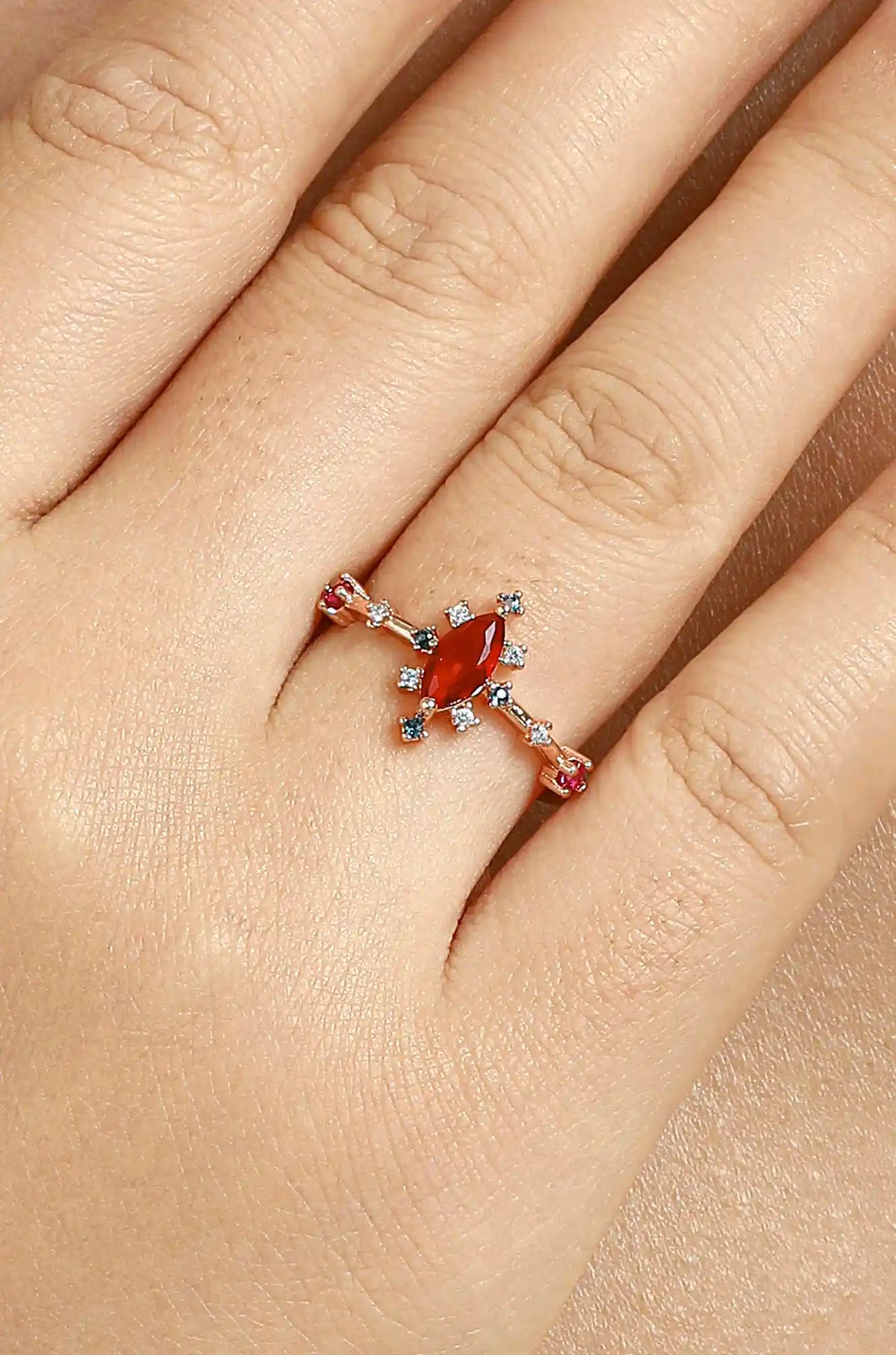 Rose gold marquise-cut ring with a red center stone worn on a finger