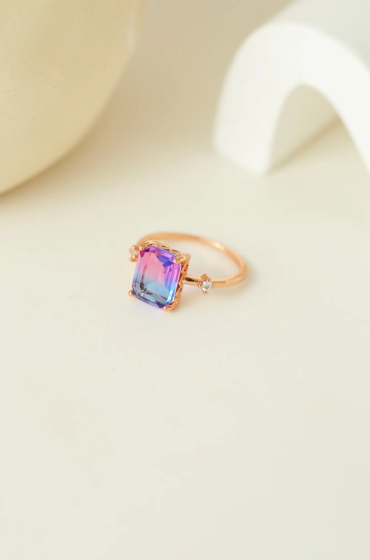 Rose gold sapphire ring with a rectangular pink-to-blue gradient center stone and side accents