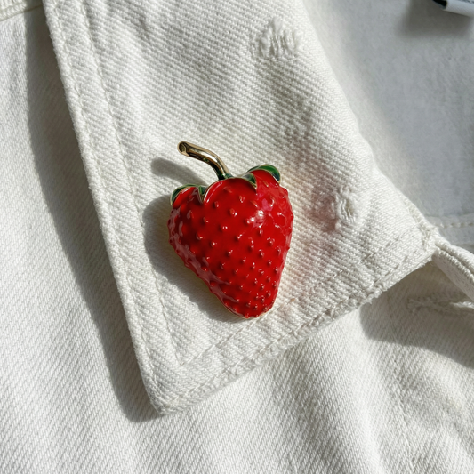 Red strawberry enamel brooch with green leaves and gold pin on white fabric