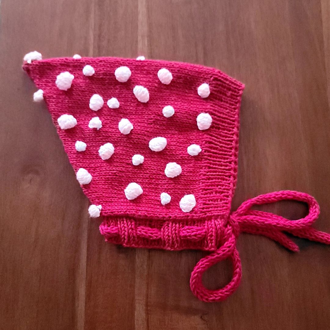 Dark red knit pixie hat with white pom-pom dots and tie