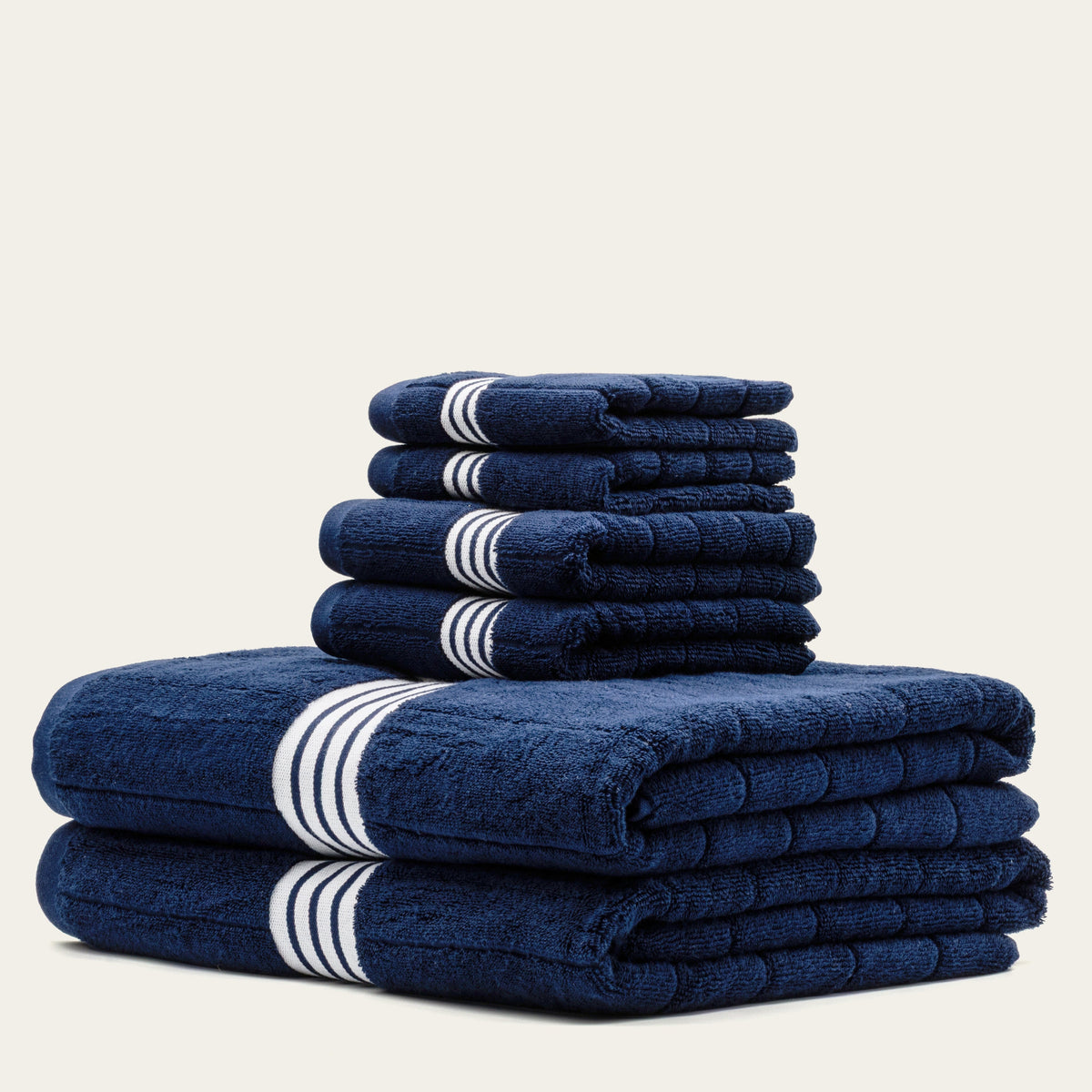Navy cotton towels with white striped bands, stacked two on one in neat folds.