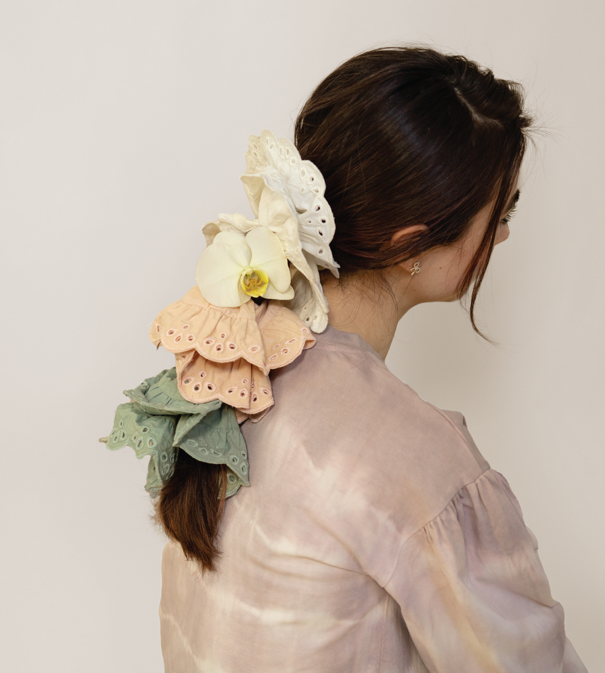 Layered eyelet scrunchies in cream, peach, and sage green, shown from behind.