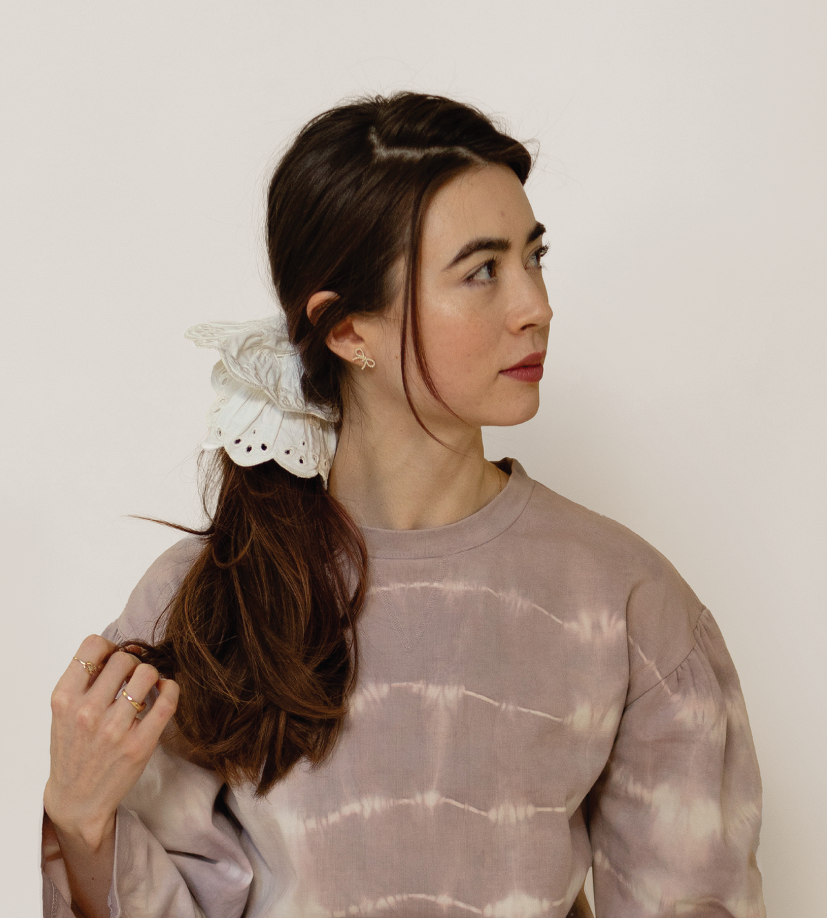 Cream eyelet scrunchie securing a ponytail, shown from the side.