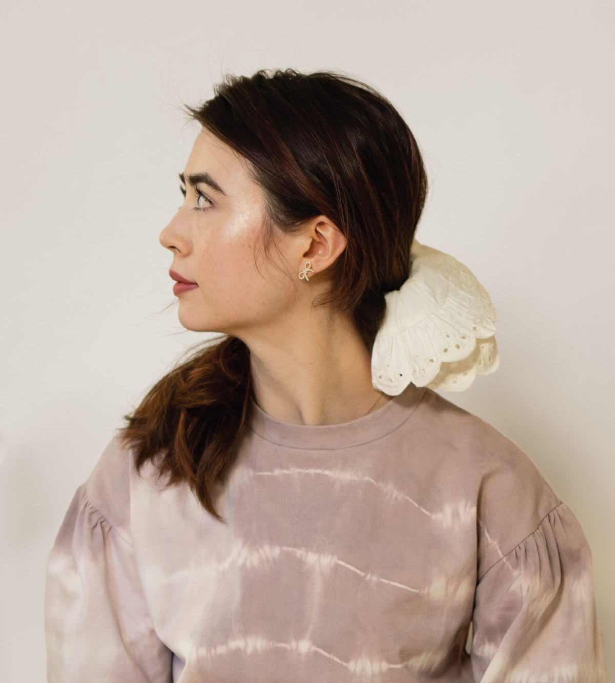 Cream eyelet scrunchie worn around a low ponytail, with scalloped edges.