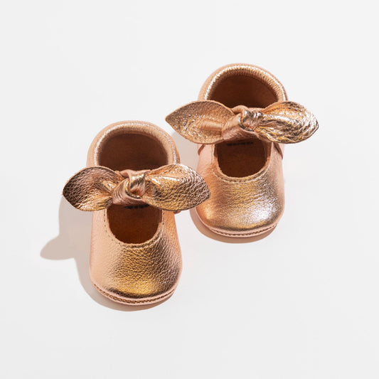 Rose gold baby shoe pair with knotted bow, soft leather-look slip-ons