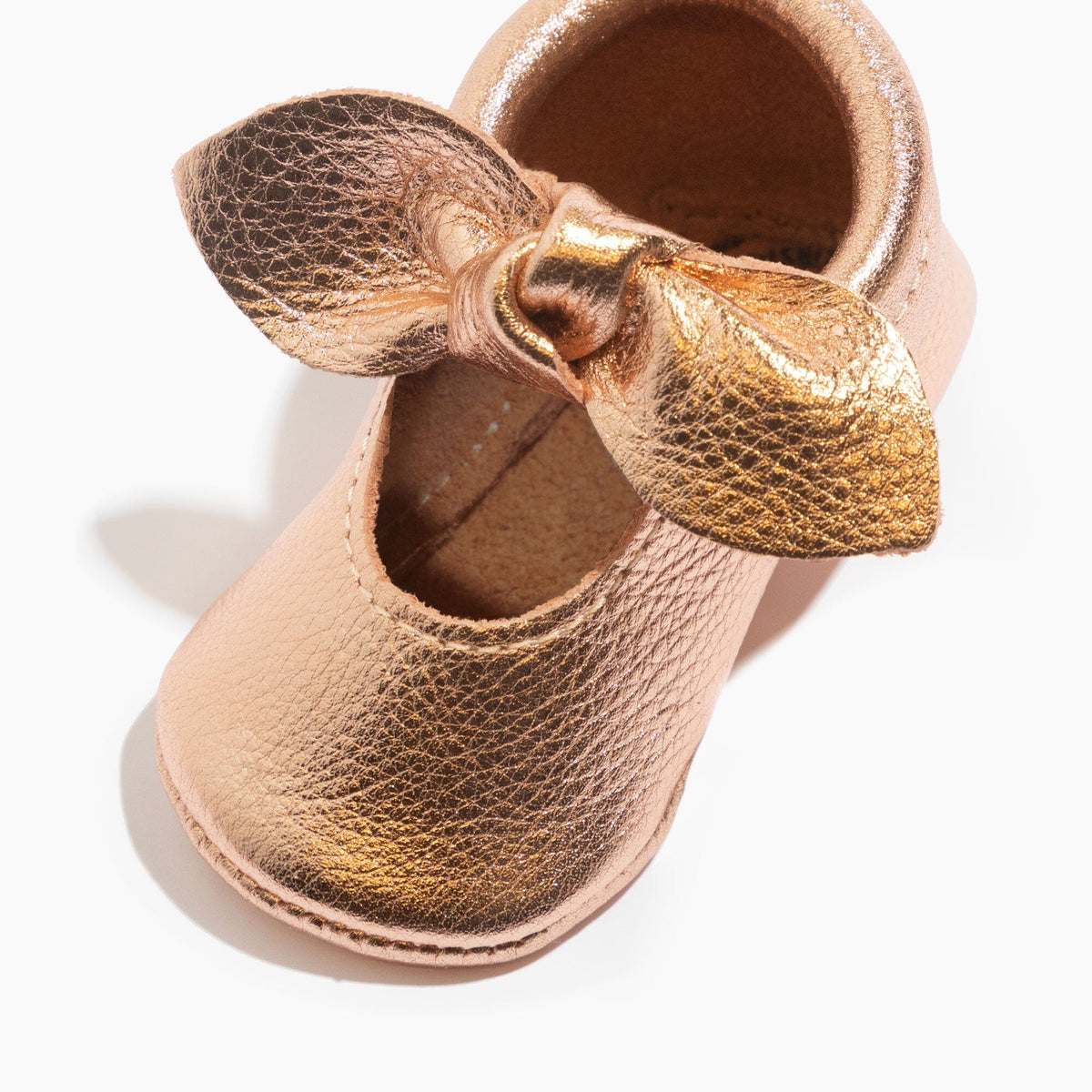 Rose gold baby shoe with knotted bow, side view, soft sole interior