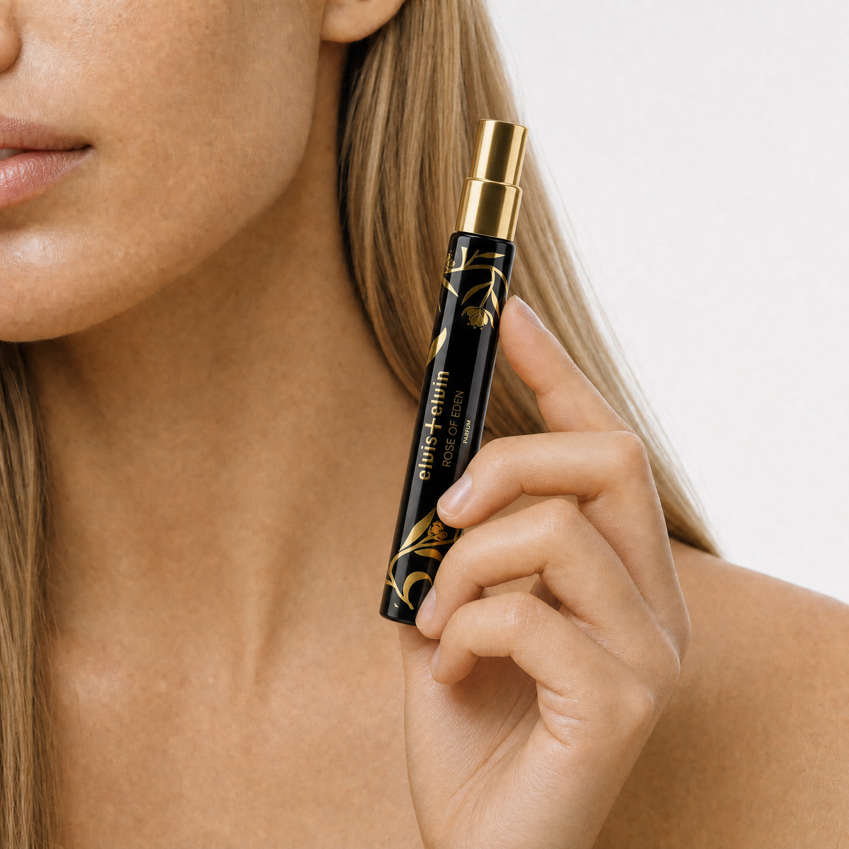 Rose of Eden perfume spray bottle held near neck, gold top and black label