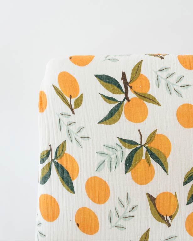 Crib sheet with white base and orange citrus with green leaf pattern, close-up