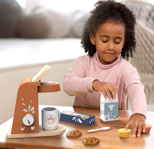 Kids' coffee machine toy on table with play cup and pods, child nearby