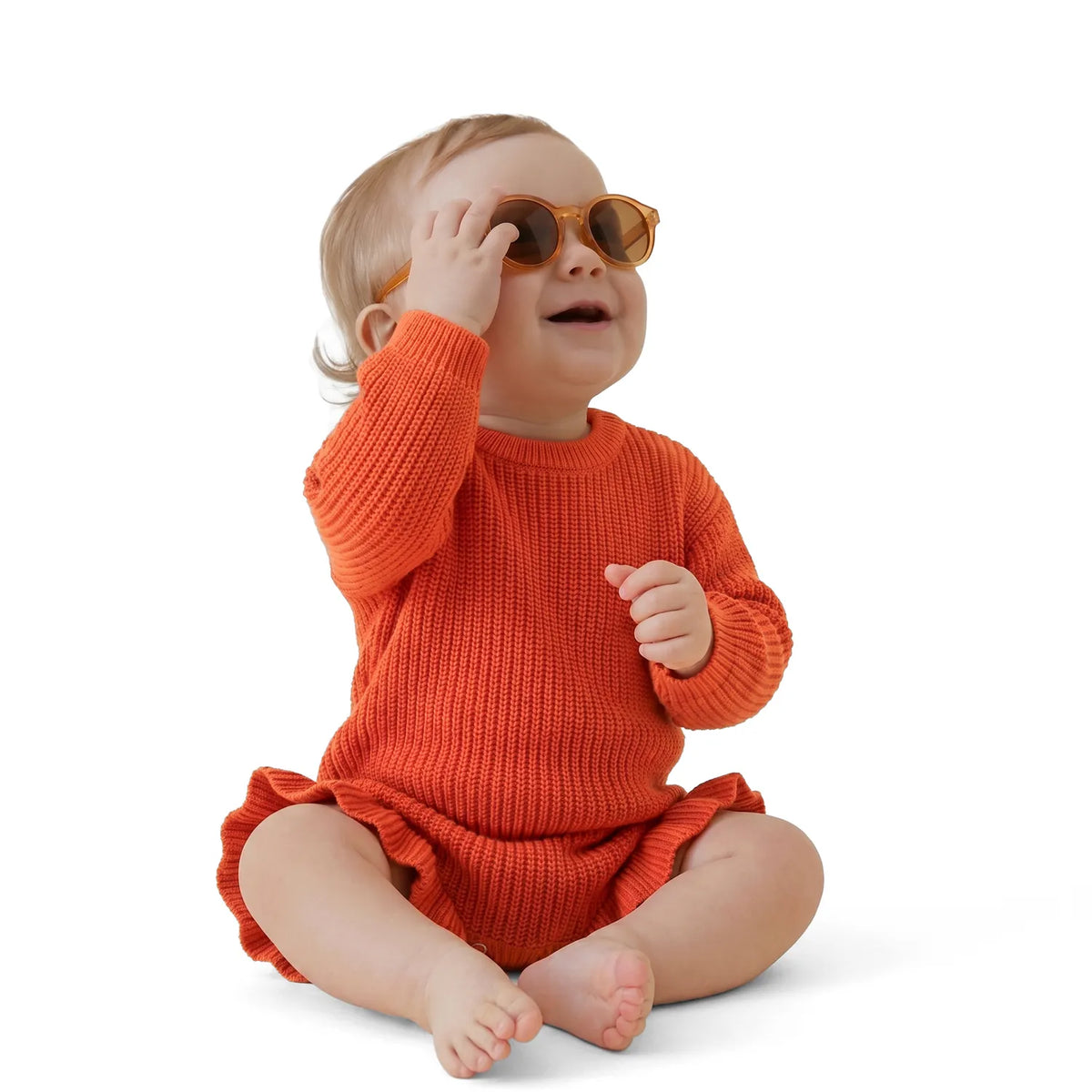 Orange-rust knit baby romper with long sleeves and ruffled cuffs, worn by baby