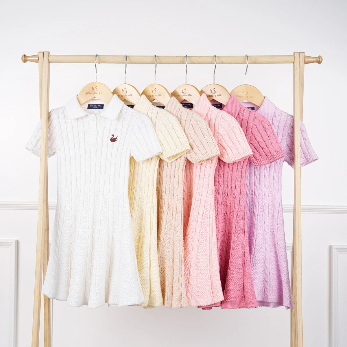 Cable-knit polo dresses on hangers in multiple colors, each with polo collar and buttons.