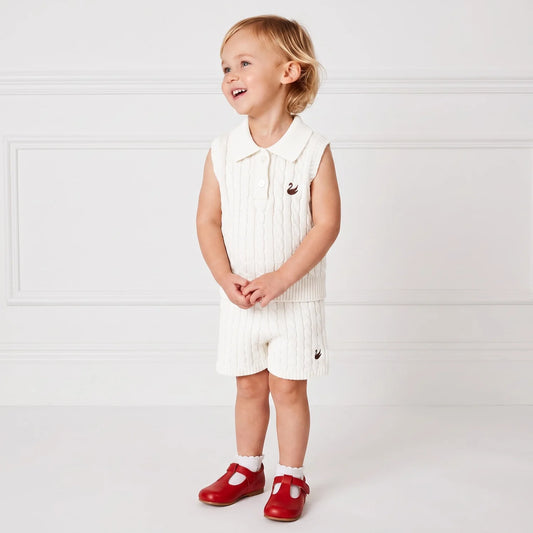 White cable-knit sleeveless short set: knit shorts with logo, worn by a child.