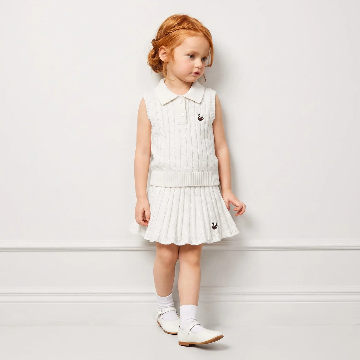 White cable-knit sleeveless polo shirt on a child, ribbed collar and buttons