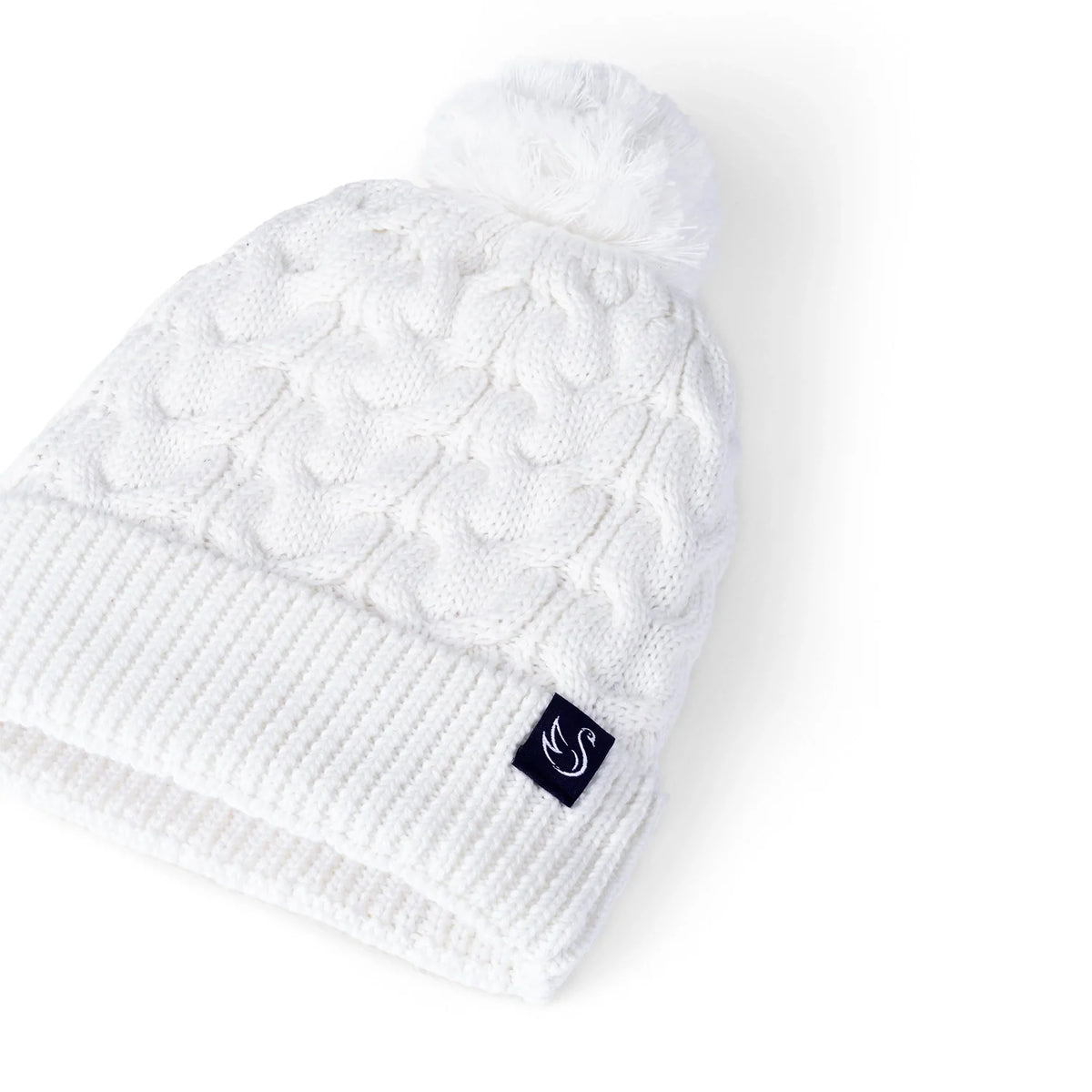 White cable knit beanie with pom-pom and dark logo patch on ribbed cuff.
