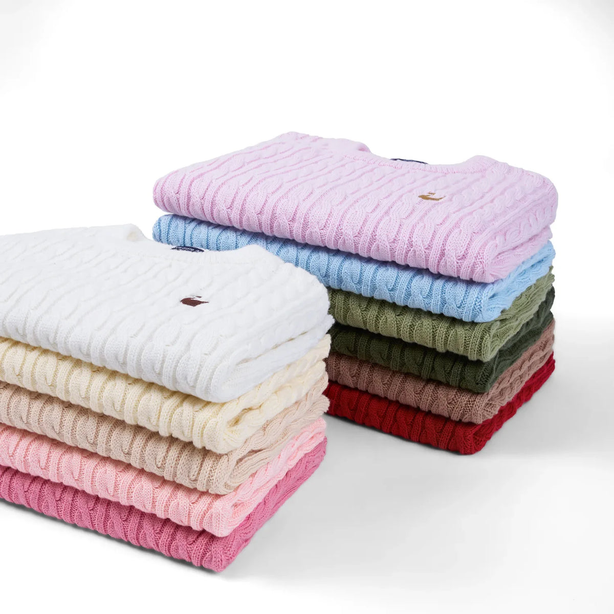 Folded baby cable-knit sweaters stack in multiple colors
