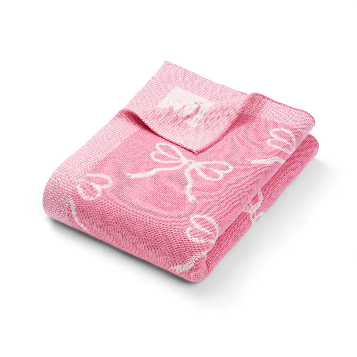 Pink knitted baby blanket with white bow jacquard pattern, neatly folded.