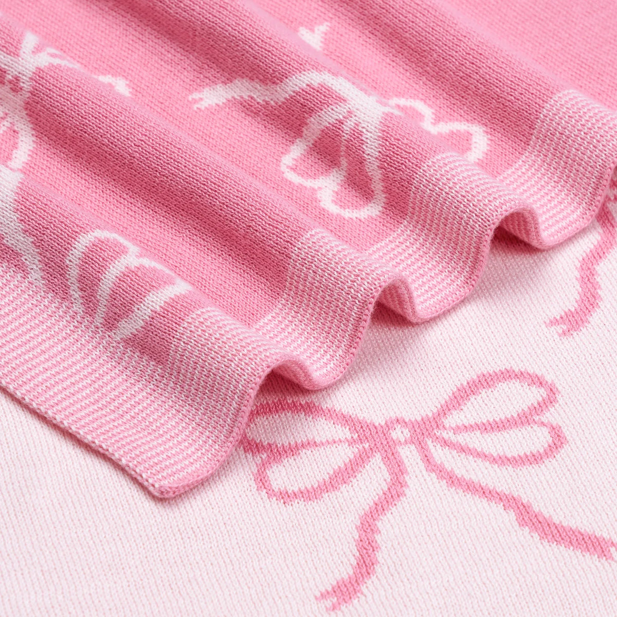 Pink knitted fabric with white bow pattern, close-up of woven texture.