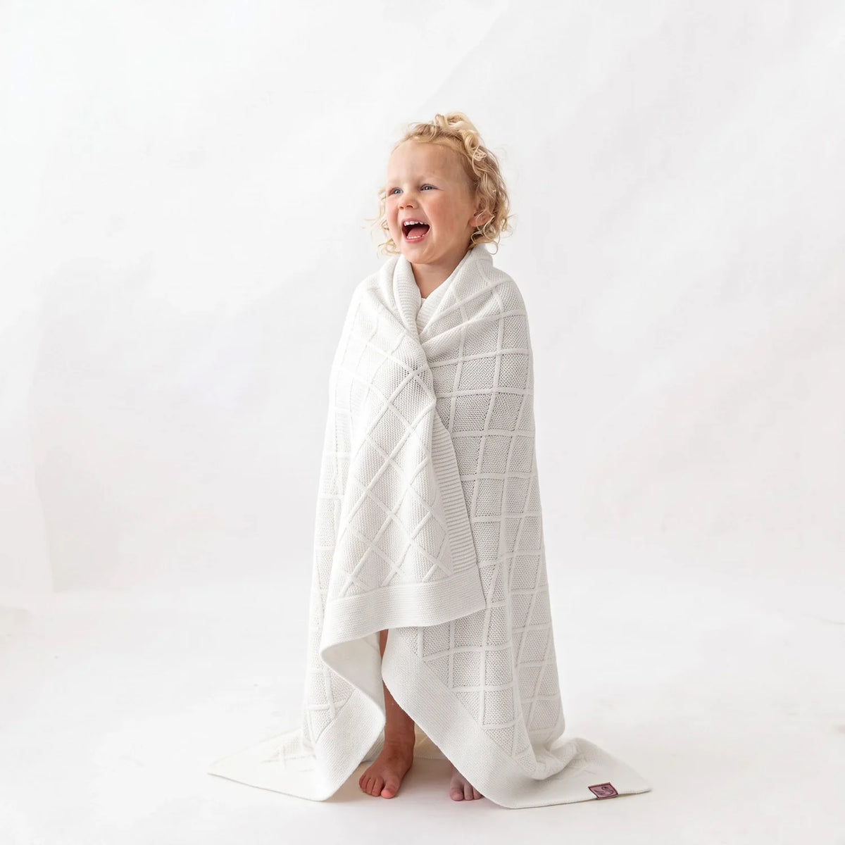 White diamond-stitch baby blanket draped as a wrap with diamond grid texture.