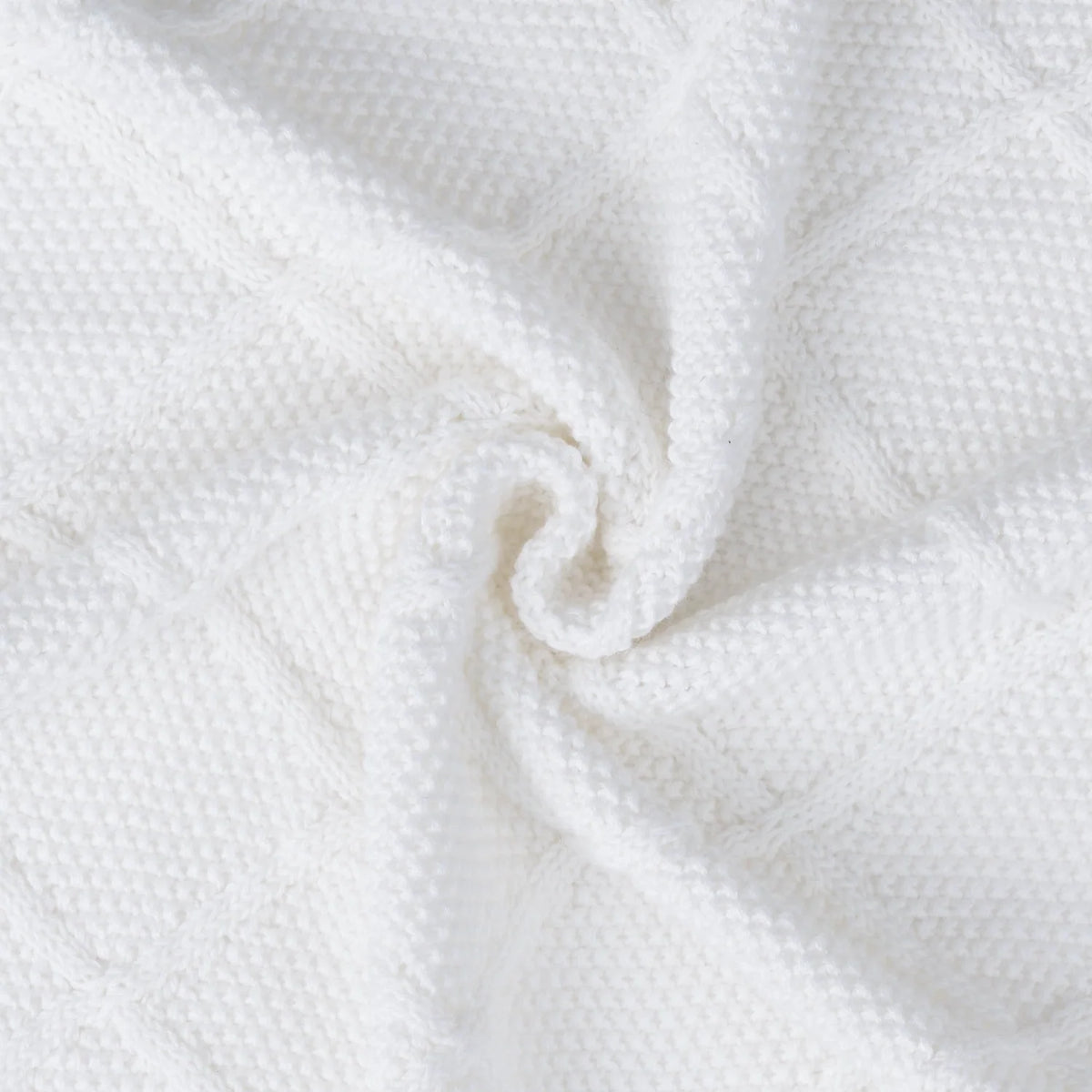 White diamond-stitch baby blanket corner close-up with gathered knit weave.