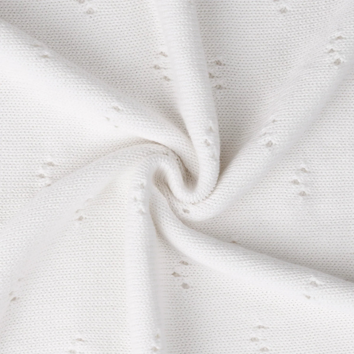 White pointelle knit blanket close-up, soft textured fabric with tiny stitched dots