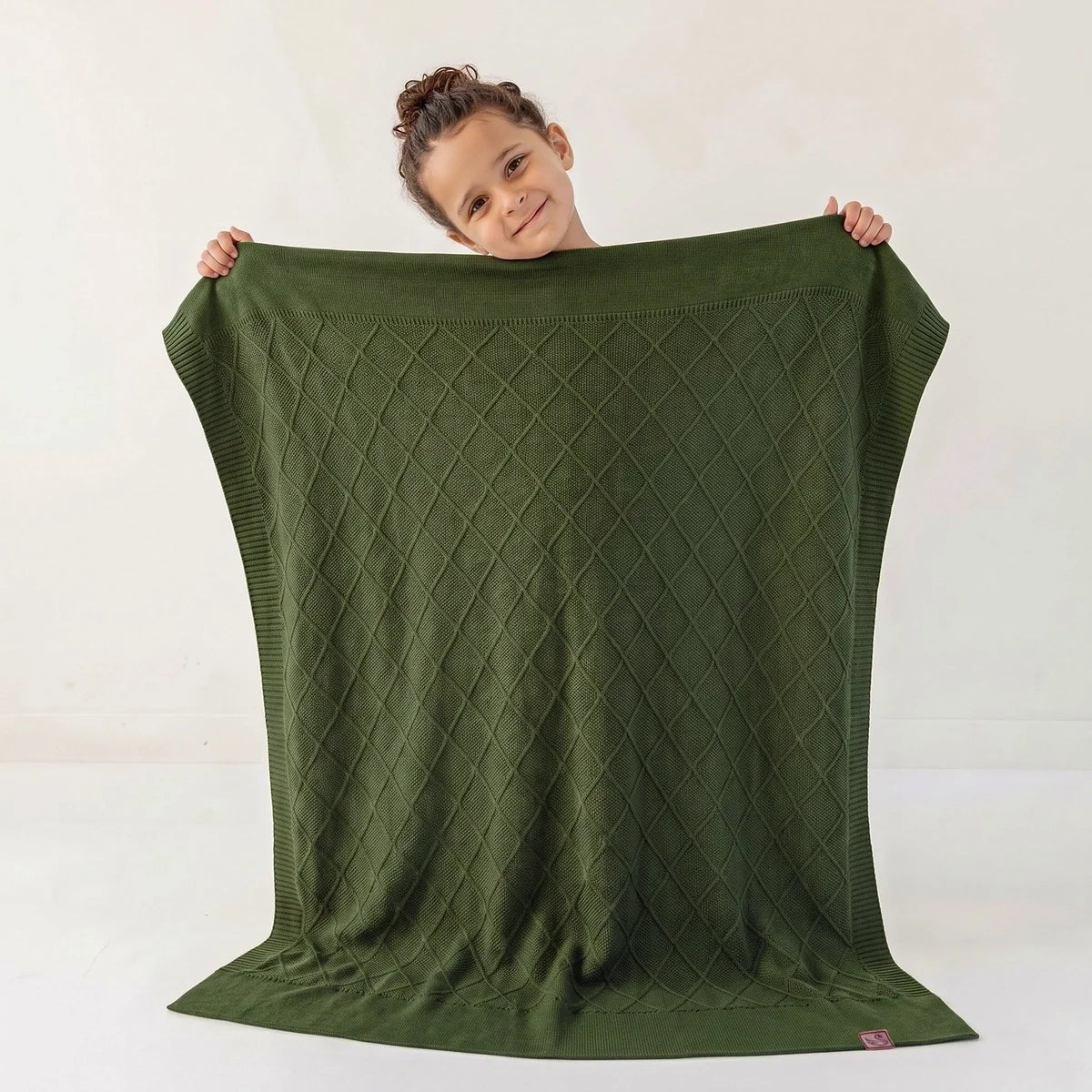 Forest green baby knit blanket with diamond stitch pattern, held up by a child