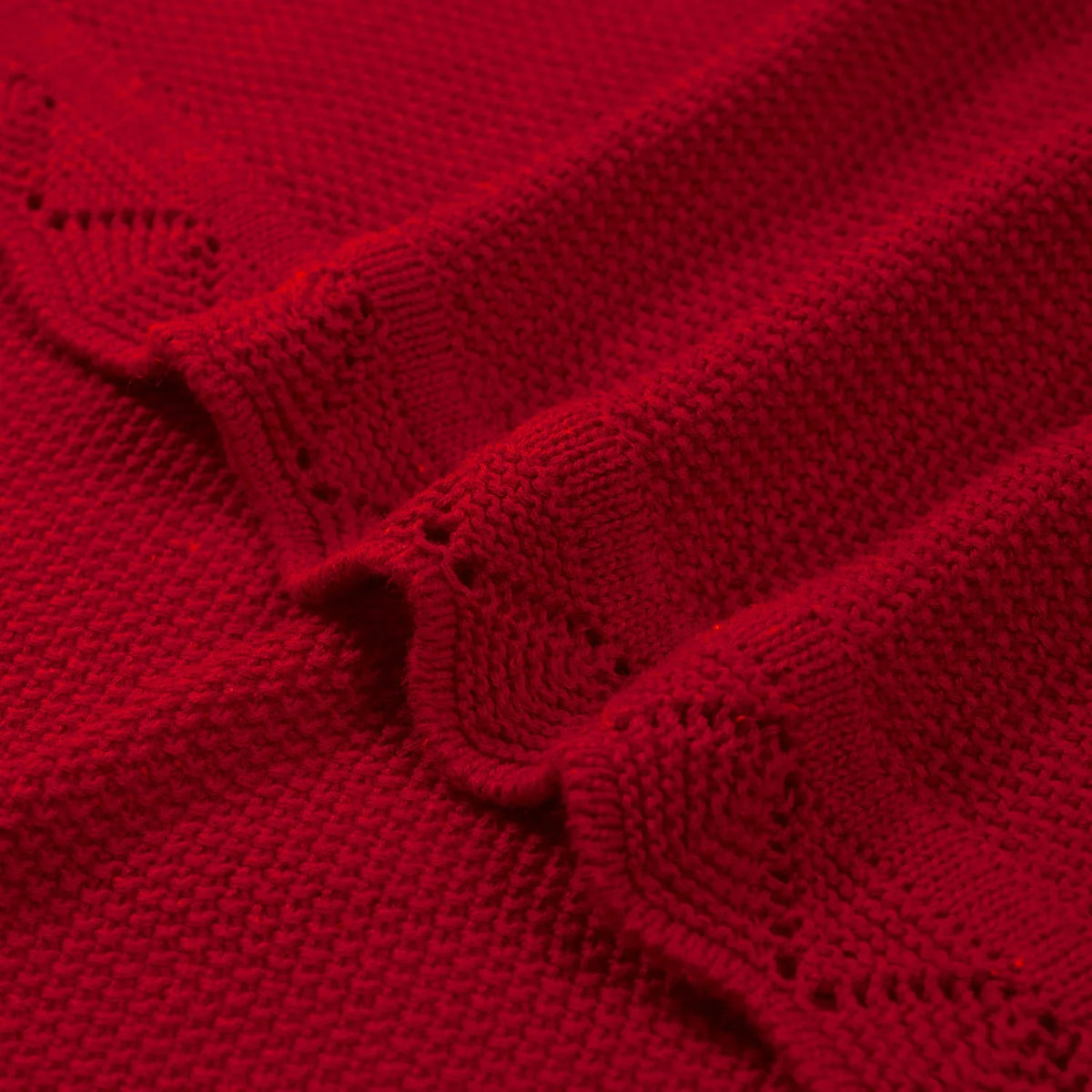 Red knit baby blanket detail with raised lace pattern and folded seam