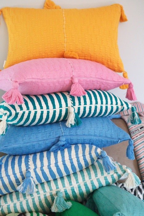 Assorted decorative pillows in orange, pink, blue, and striped aqua with tassels