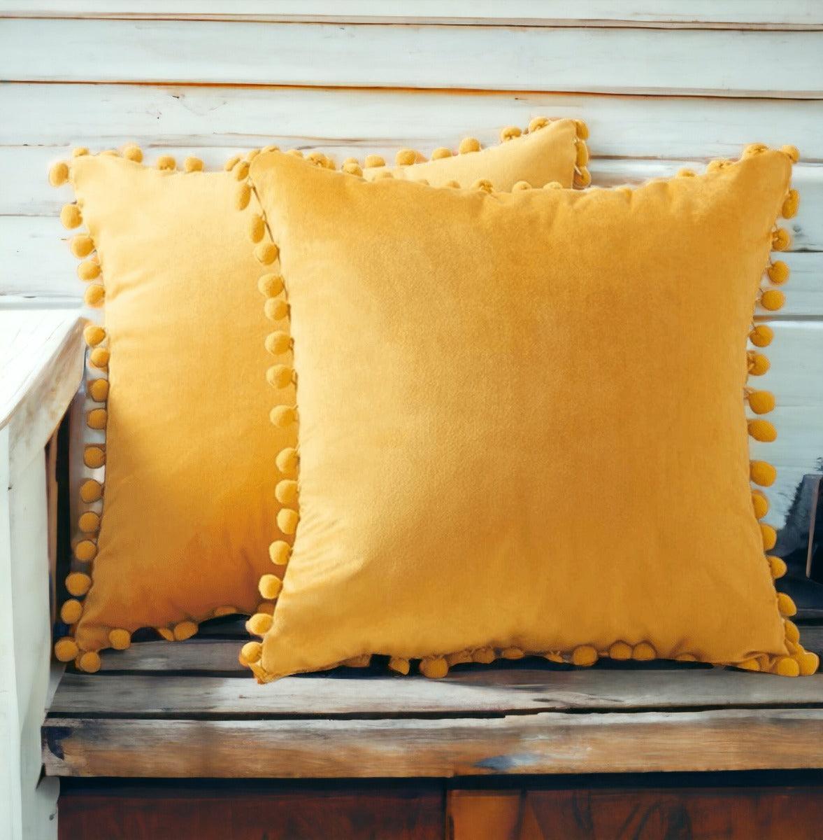 Yellow plush throw pillow with rounded pom-pom trim on a bench