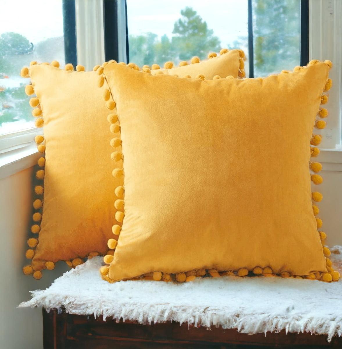 Yellow plush throw pillow with pom-pom trim along the border