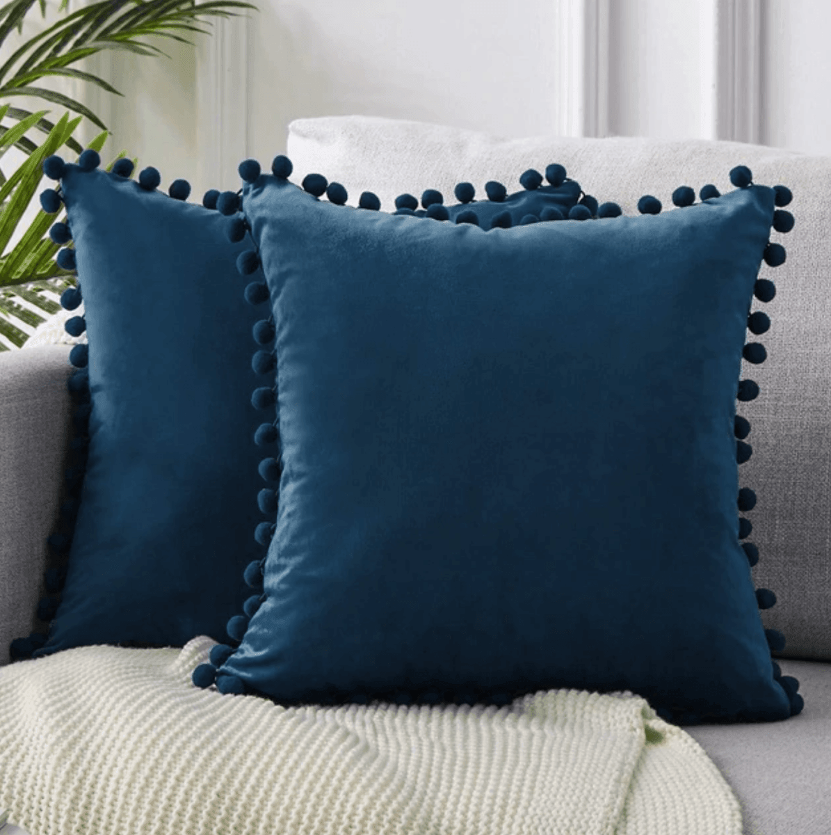 Dark blue plush throw pillow with pom-pom trim around the border