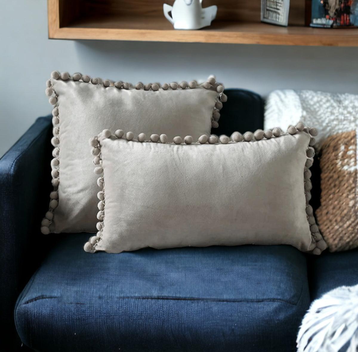 Gray plush throw pillow with pom-pom trim around the edges
