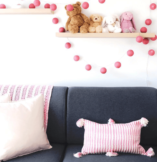 Faded pink striped lumbar pillow with corner tassel pom-poms on a couch