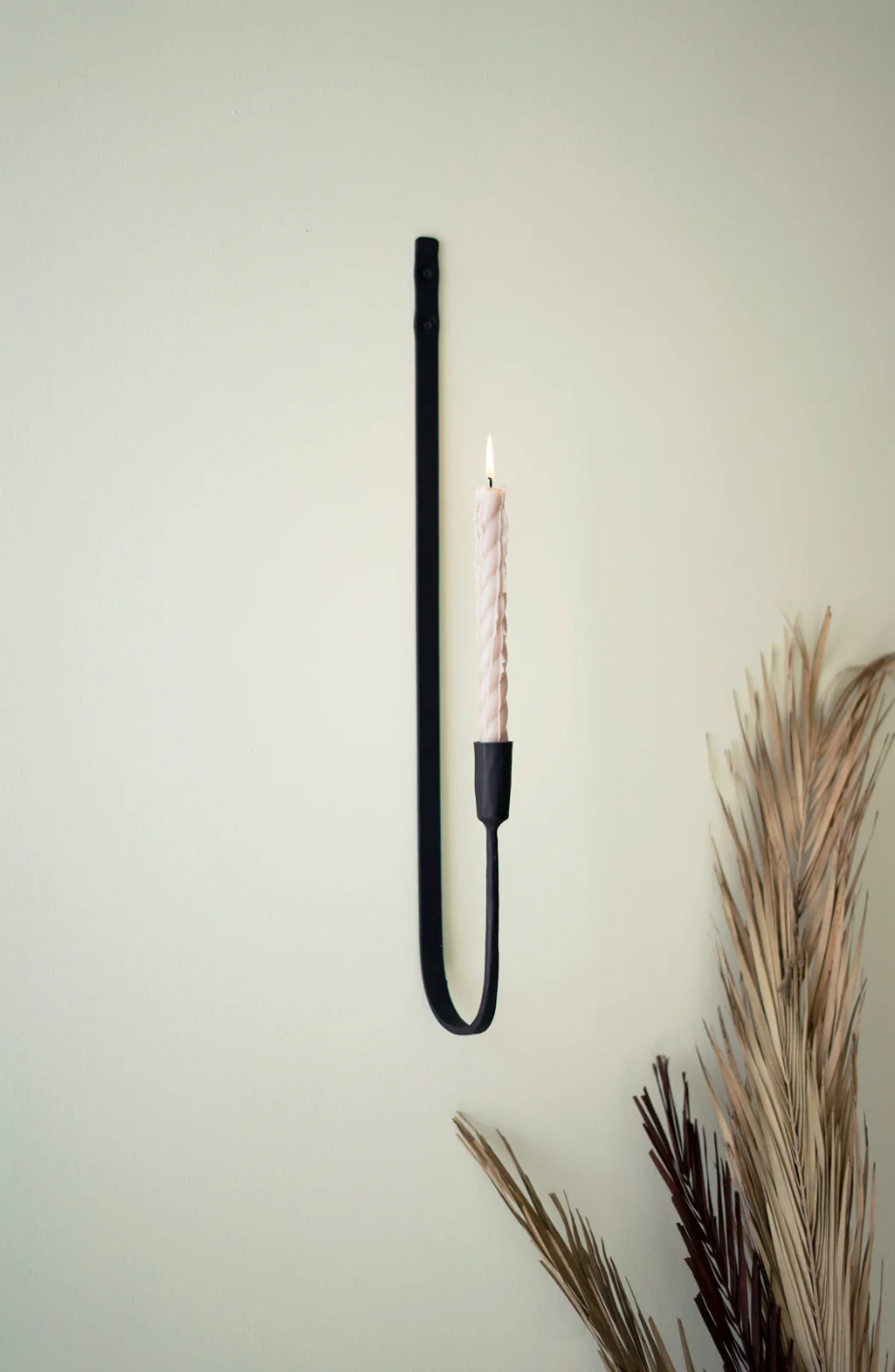 Black iron wall sconce with single lit candle