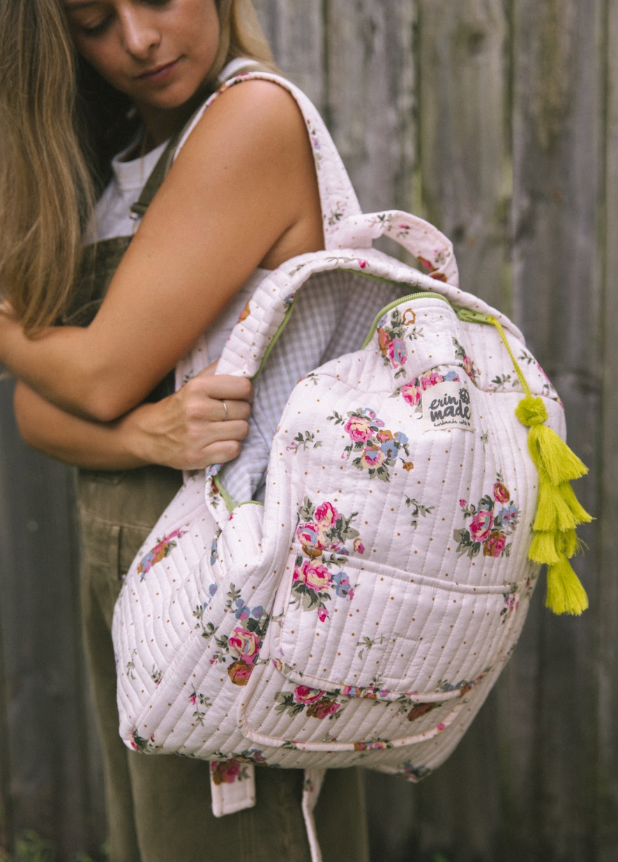 Light pink quilted floral backpack with open top compartment and yellow tassel charm