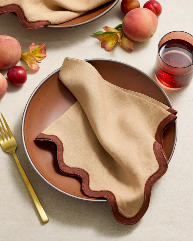 Beige linen napkin with scalloped edge and dark brown border, folded