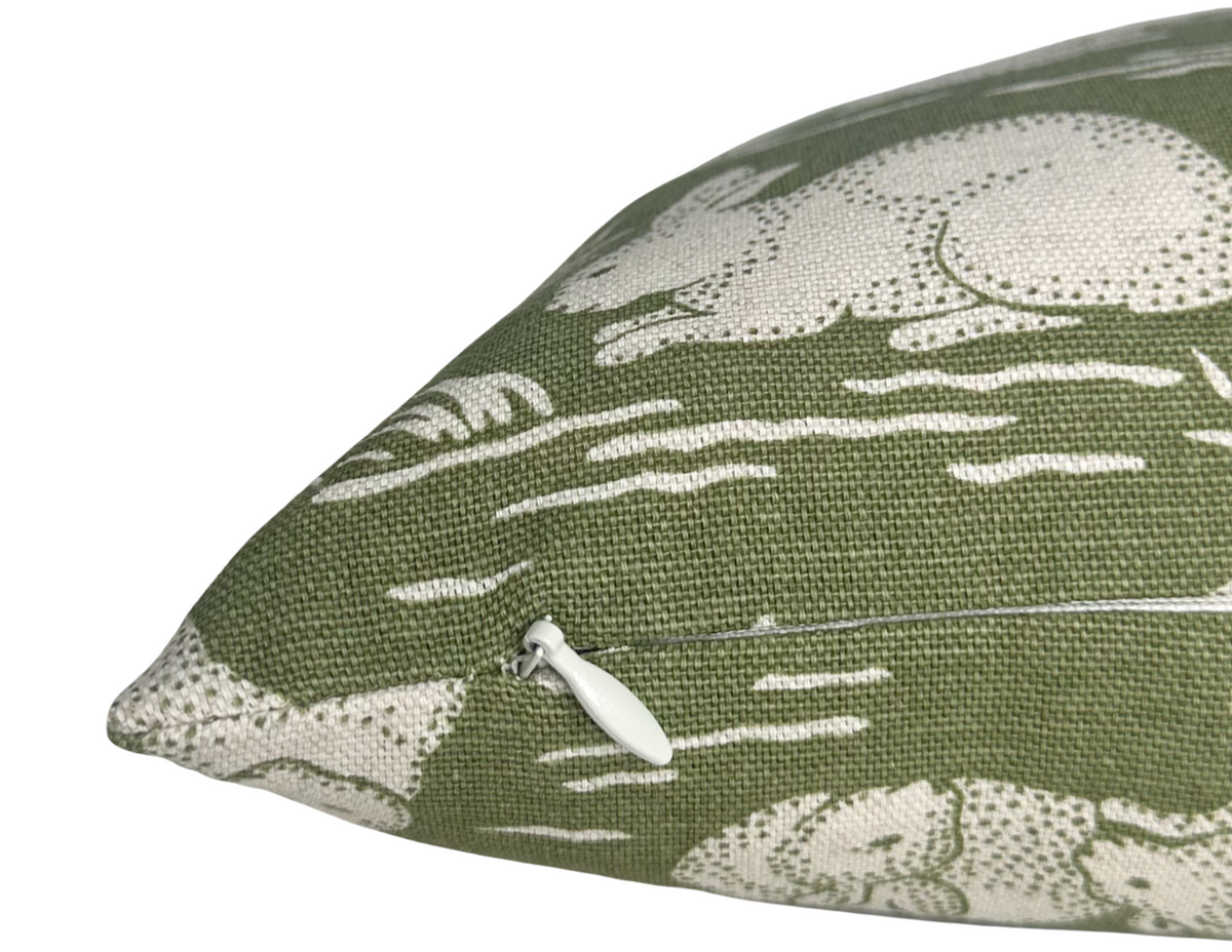 Corner detail of sage green cotton pillow cover with white rabbit print and piped trim