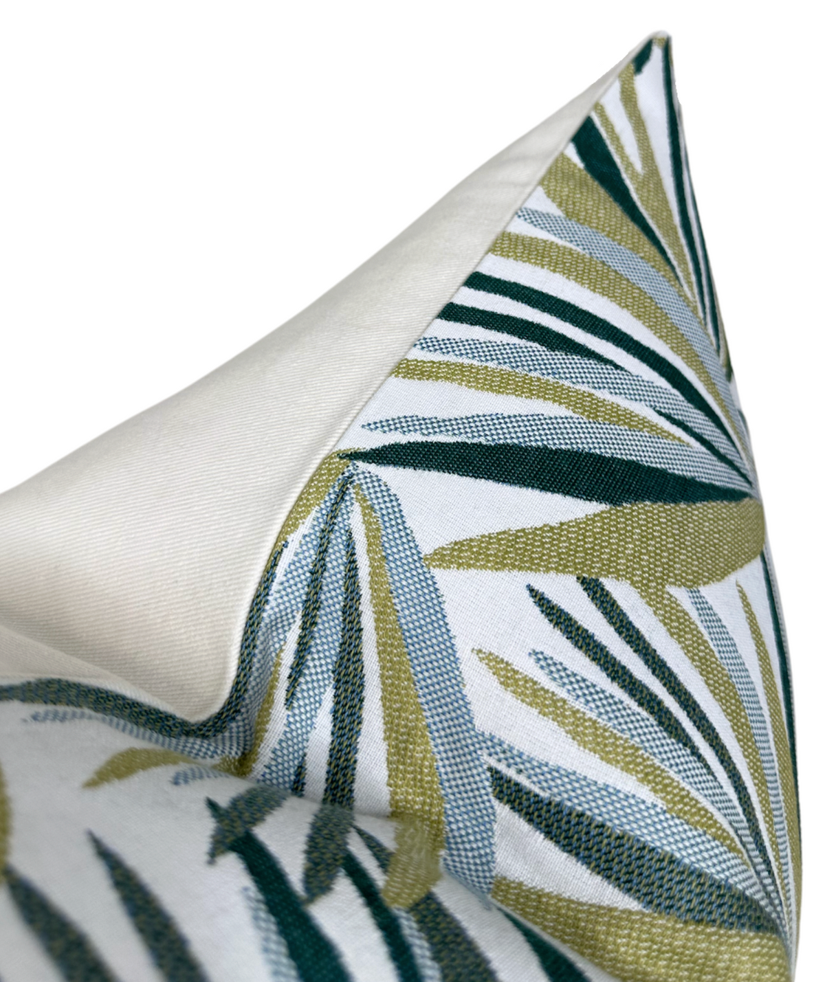 Pillow cover detail with tropical leaves in teal and green over a light background; corner view.