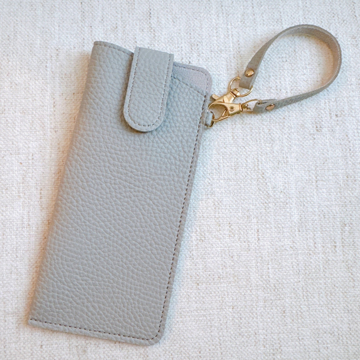 Light gray bag charm glass case with wrist strap and gold-tone clasp