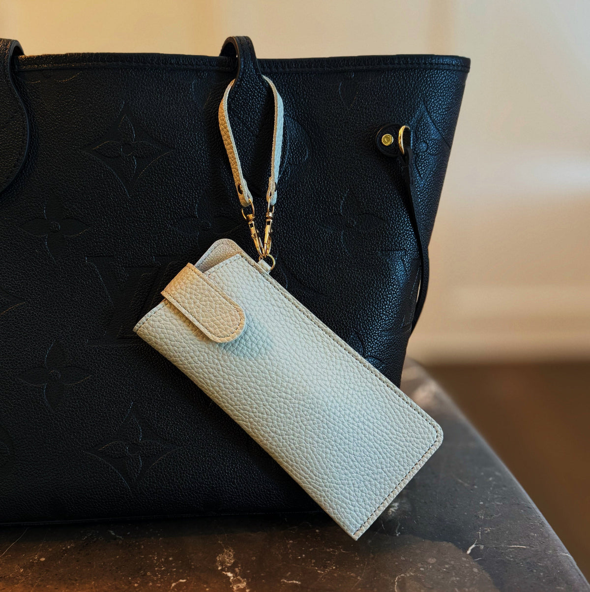 Cream bag charm glass case with wrist strap attached to a black bag