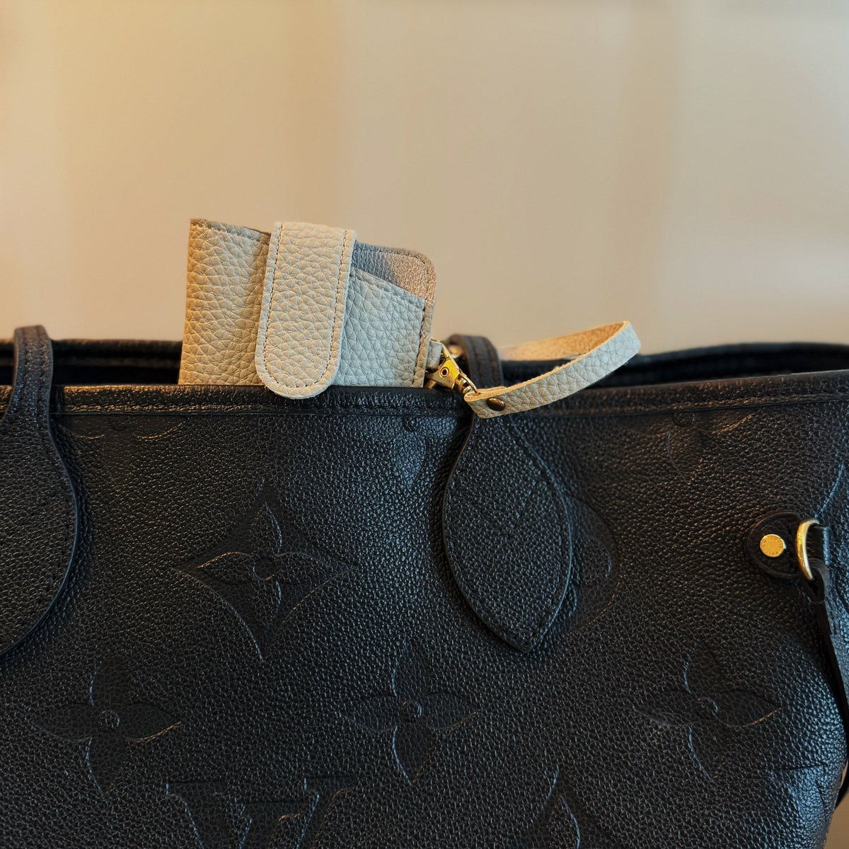 Light-colored bag charm glass case with wrist strap attached to a black bag