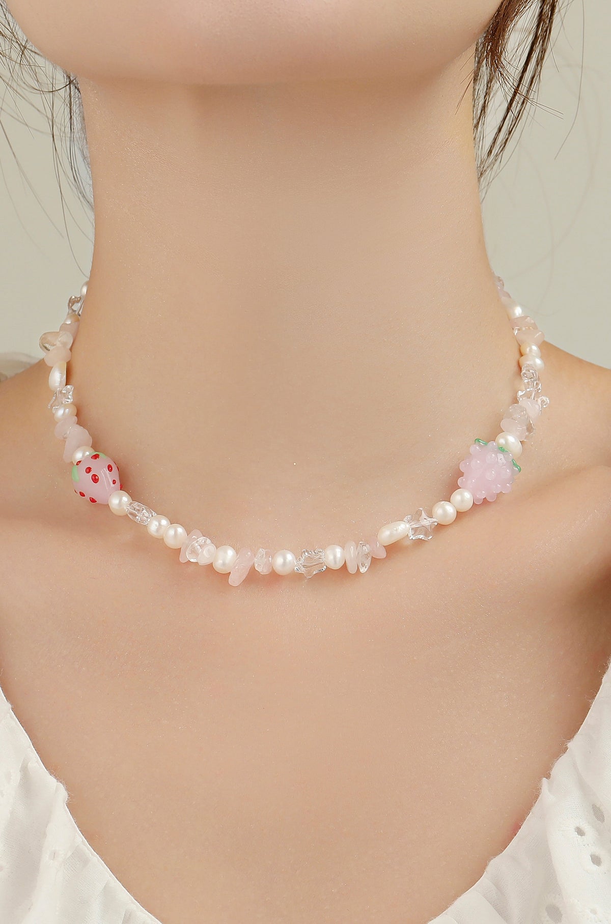 Strawberry necklace worn at the neck, with pale beads and pink strawberry charms