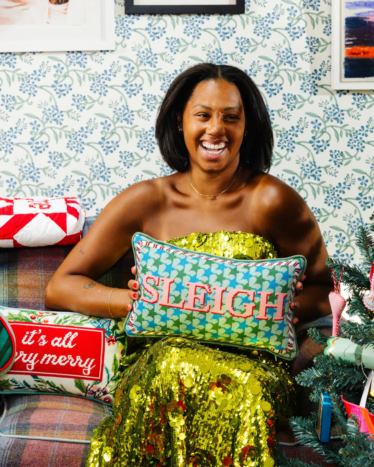 Holiday pillow with teal patterned cover and red 'SLEIGH' lettering, held by person