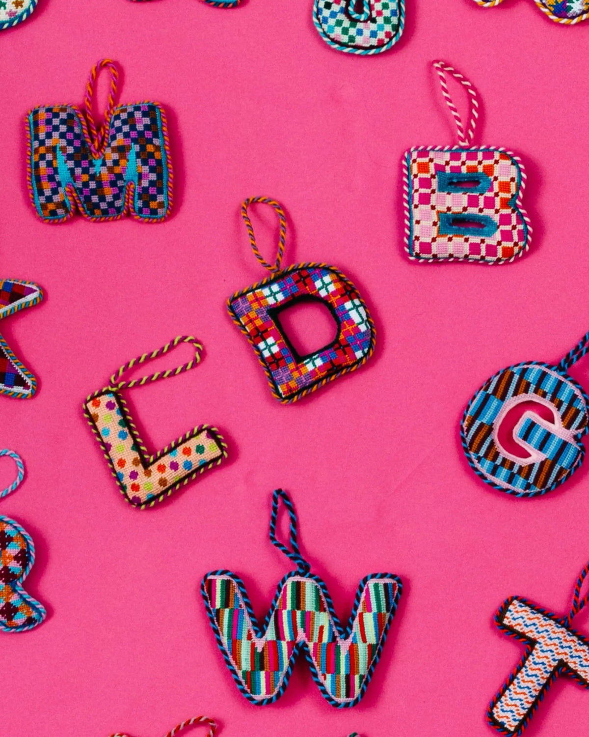 Needlepoint monogram letter ornaments with multicolor plaid stitched patterns and hanging loops