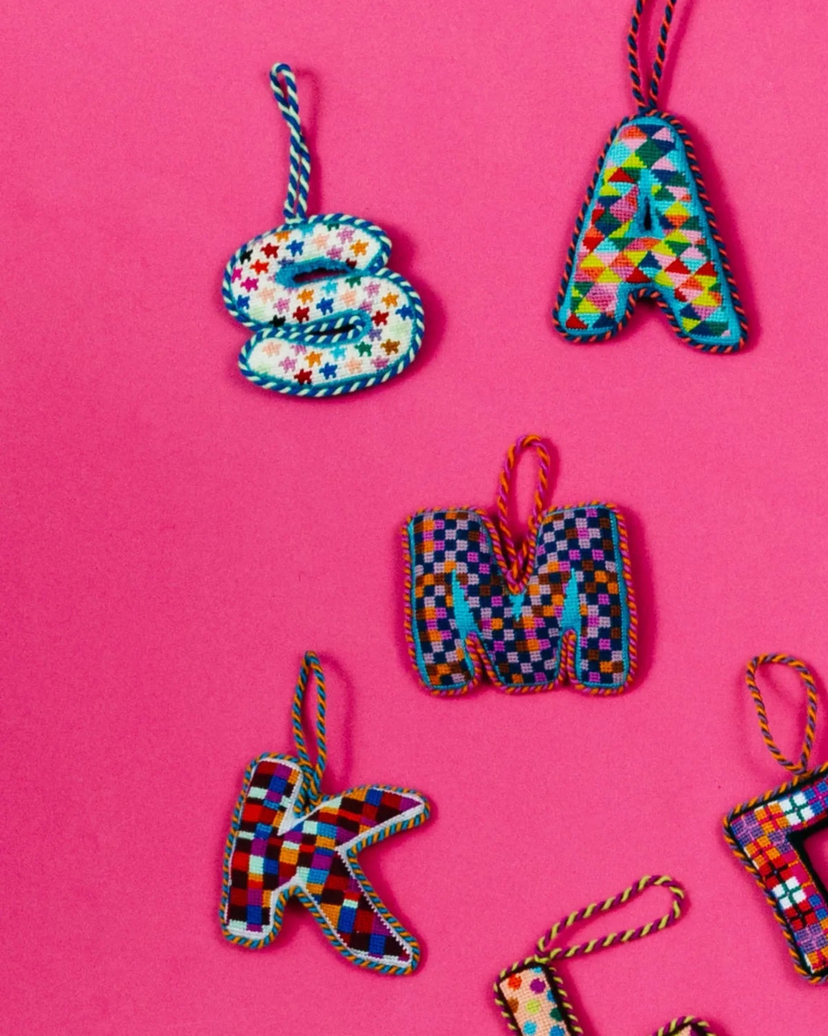 Needlepoint monogram ornament with multicolor stitched pattern and hanging cord.