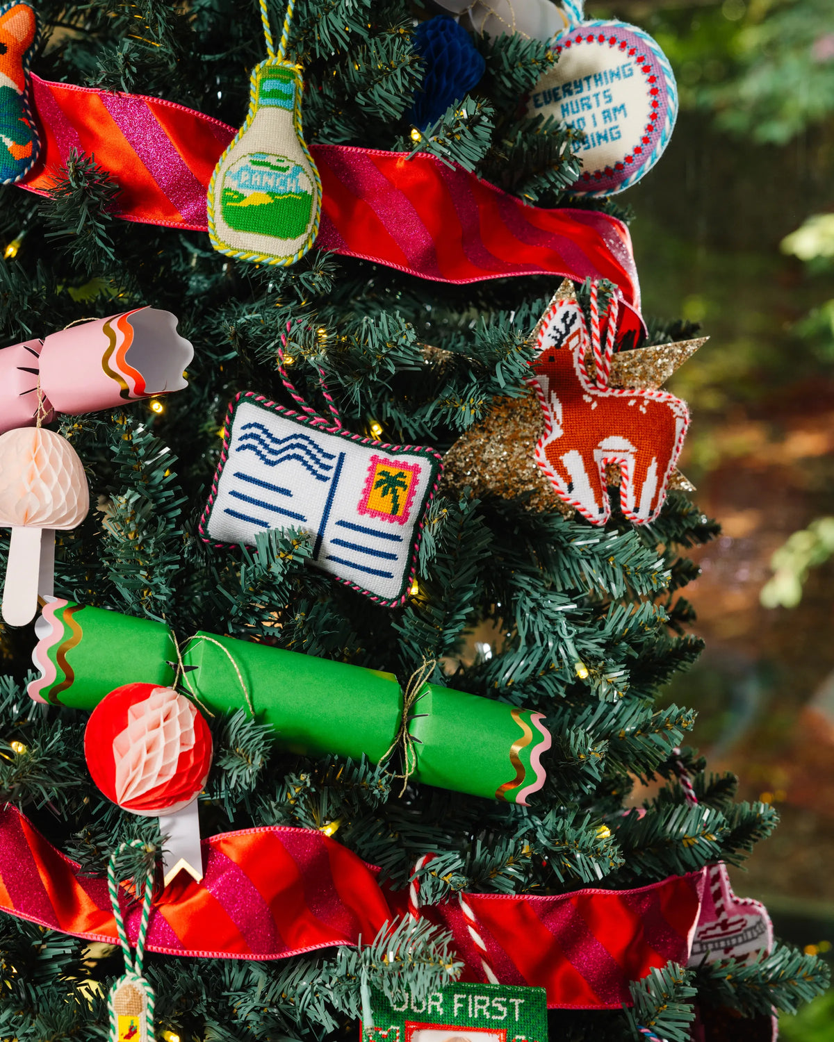 Needlepoint open-book postcard ornament hanging on Christmas tree, red green trim
