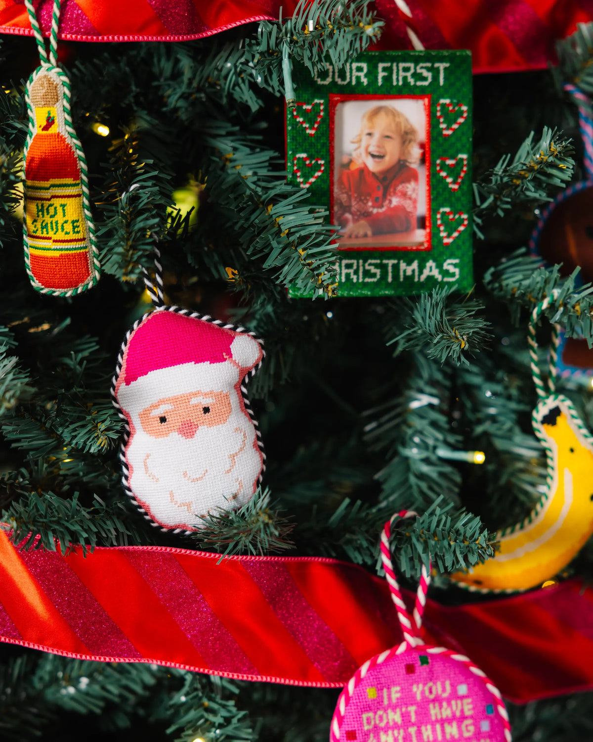 Hanging green photo frame ornament reading “Our First Christmas” on a Christmas tree