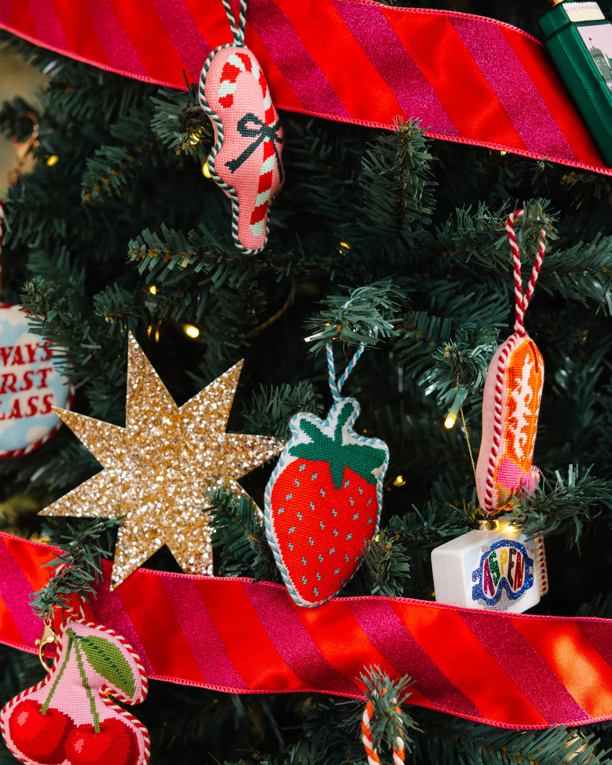Needlepoint strawberry icon ornament hanging on a Christmas tree among decorations
