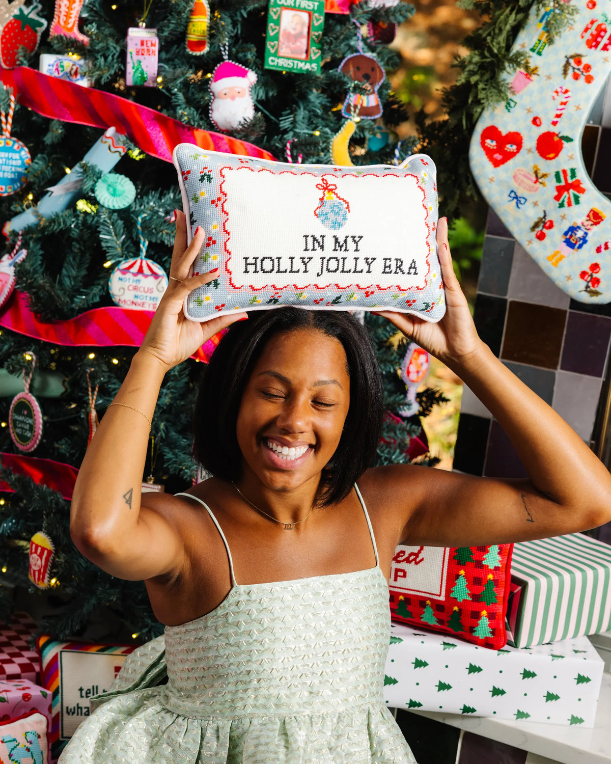 Needlepoint pillow held up with 'IN MY HOLLY JOLLY ERA' stitched lettering
