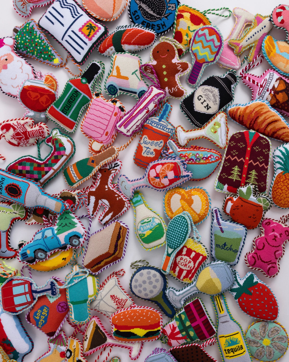 Assorted needlepoint ornaments with colorful stitched designs, many looped for hanging.