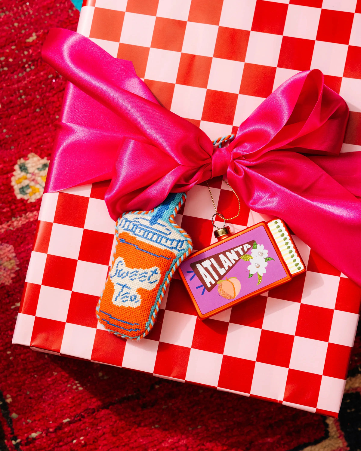 Needlepoint bottle ornament hanging from a bright pink bow on a gift box